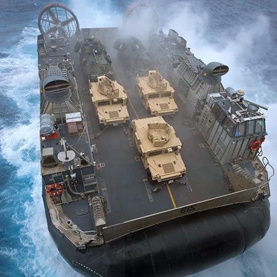 Aerial view of giant military hovercraft with mobile antennas at sea carrying three humvees 