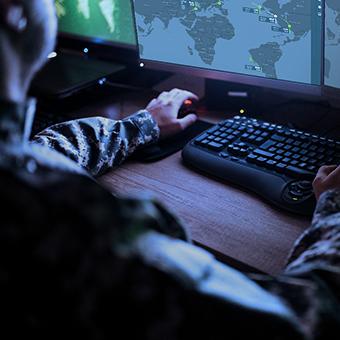 Military man sitting at a desktop computer looking at a map of the world on a monitor