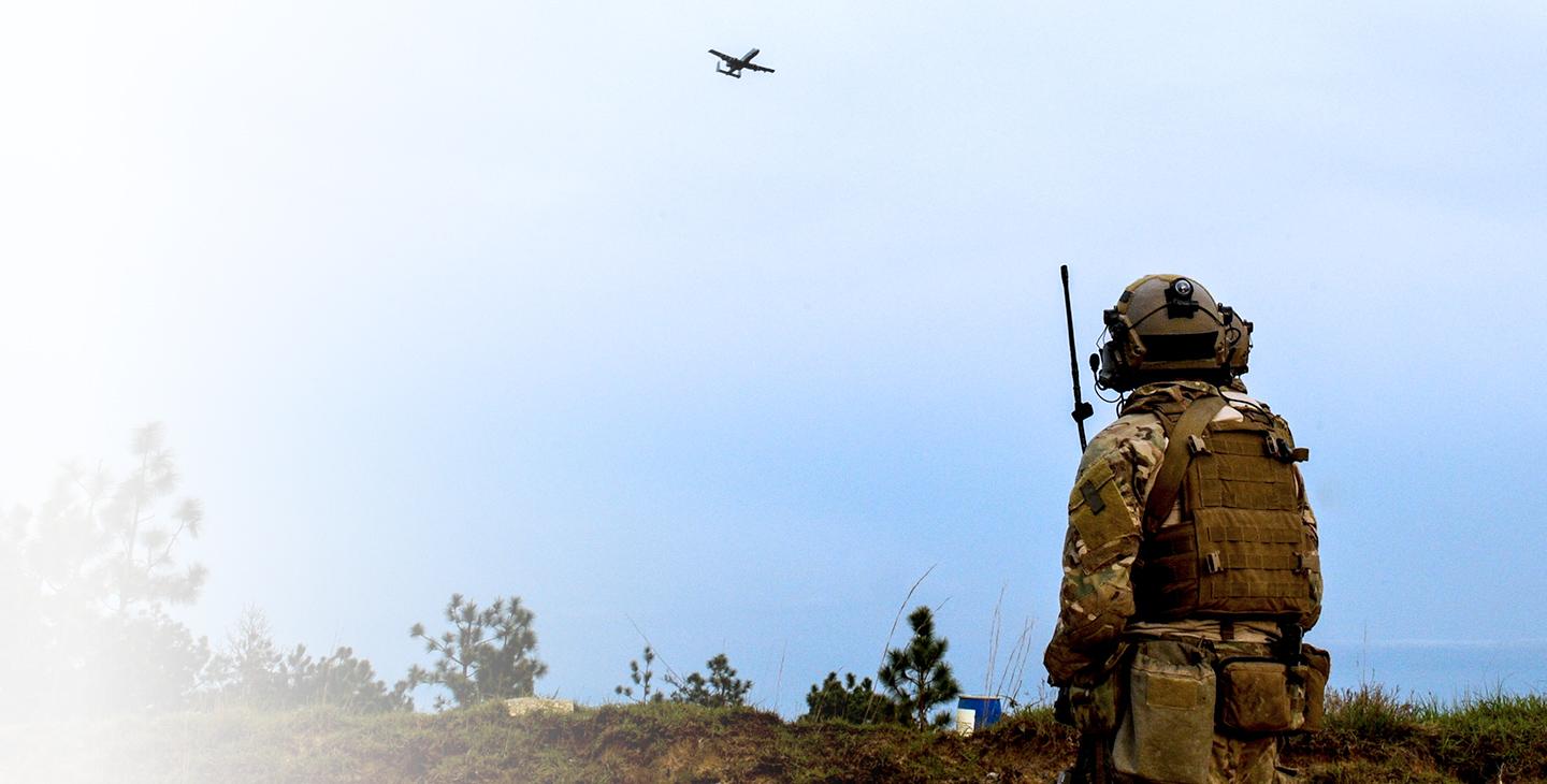 JTAC的作战人员在战场上拿着军用卫星通信天线仰望一架飞过的飞机