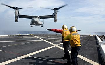 2 man flight crew helping a military plane land on a ship at sea