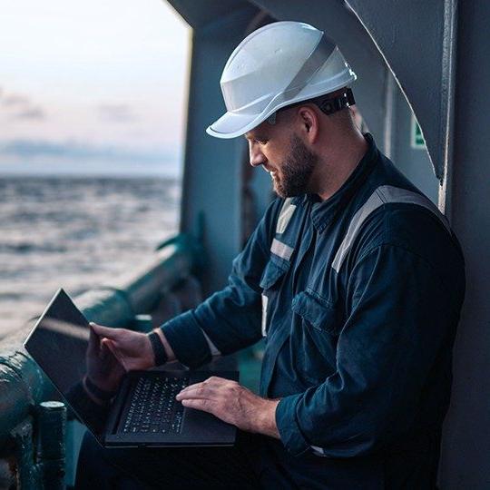 一名戴安全帽的男子在海上的船上用笔记本电脑上网.